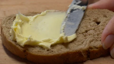 Close-up butter spreading on rustic rye bread with metal knife on wooden table Video stock 142185785