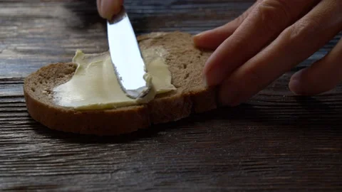 Close-up butter spreading on rustic rye bread with metal knife on wooden table Stock Footage 142983120