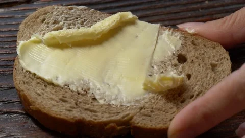 Close-up butter spreading on rustic rye bread with metal knife on wooden table Stock Footage 146568389