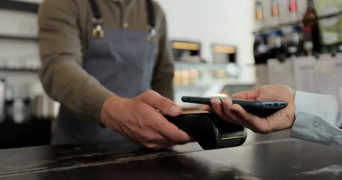 Close up in the cafe man makes takeaway coffee for a customer who pays by Stock Footage 159556469