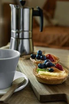 Close-up of a cake with fruit, cup of coffee and coffee pot in the background Stock Photos