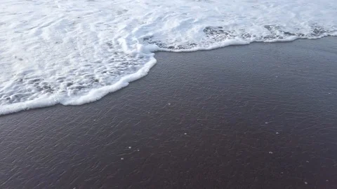 Close up of calm ocean waves foam slowly covering sand on beach during bright Video stock 123035958