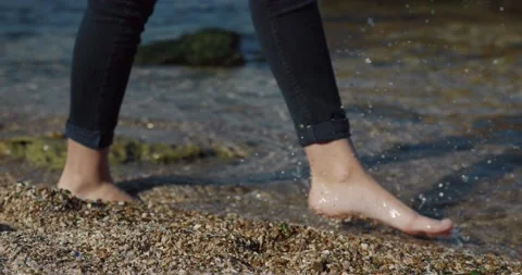 Close up of camera follows legs in jeans. Female legs walk barefoot on the sea Stock Footage 147060748