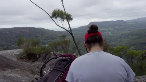 Close-Up Camera Rotation Behind Woman Sitting on Cliff Overlooking Valley Stock Footage 329367342