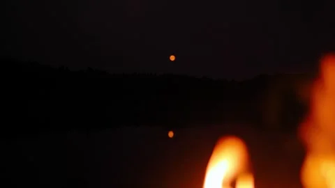 Close-up of campfire against the moon reflected in the water in the evening. Stock Footage 283081994