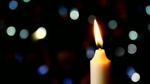 Close up of Candle Flame flickering in front of Christmas Holiday lights. Stock Footage 98969444
