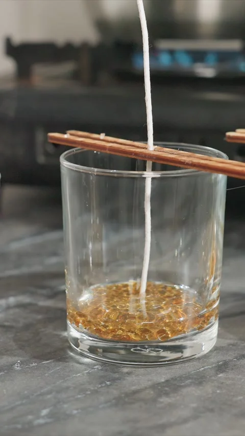 Close up of candle making process showing wick dipping into golden paraffin wax Stock Footage 344673070