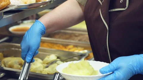 Close-up, canteen worker lays a portion of mashed potatoes on the plate. in Video stock 103579700