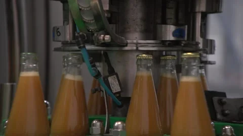 Close up of capping orange-colored juice bottles inside bottling line Stock Footage 163892375