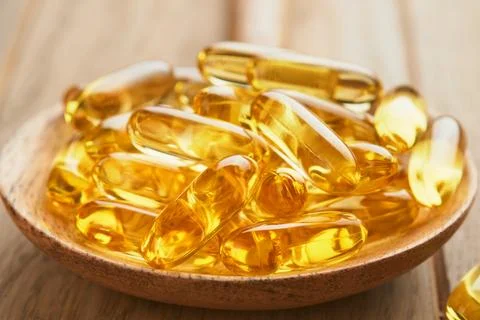Close up capsules with Vitamin D, E or Omega 3,6,9 fatty acids in bottle on o Stock Photos