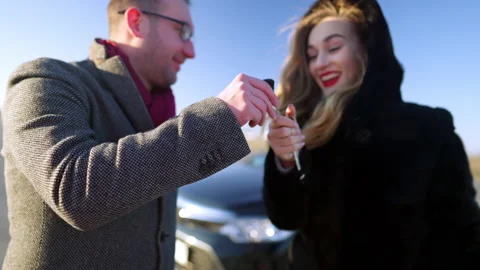 Close-up of car key with blurred rich man presenting gift to excited young woman Stock Footage 148766027