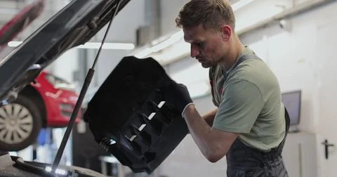 Close up of car mechanic removes the engine cover of a car and inspects the.. Stock Photos