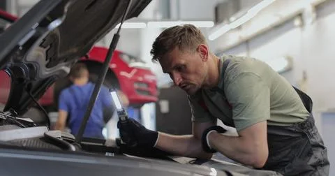 Close up of car mechanic removes the engine cover of a car and inspects the.. Stock Photos