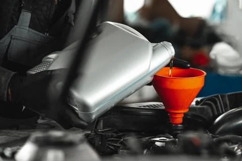 Close up of car service worker pouring new oil into car engine 写真素材
