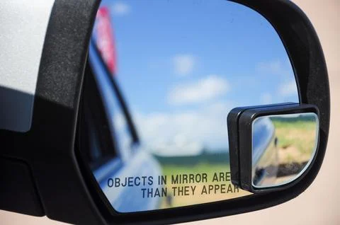 Close-up of a car side mirror reflecting the blue sky and distant landscape. Foto stock