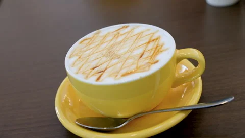Close-up of a caramel latte in a yellow cup on a wooden table Stock Footage 340521542