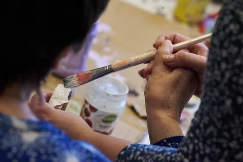 Close up of a caregiver's hands helping an elderly person paint a small craft 库存照片