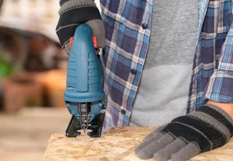 Close up the carpenter ware gloves cutting wood sheet by electric jigsaw. Stock-Fotos