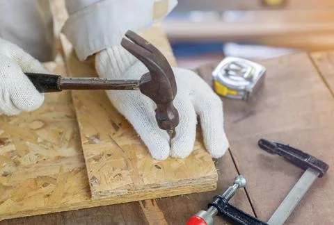 Close up the carpenter ware white gloves hold hammer hit nail on oriented str Foto stock