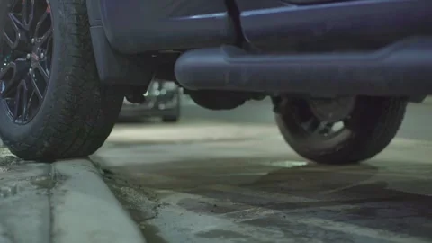 Close-up of a car's back wheels as it backs up onto a sidewalk curb. The Stock Footage 257693371