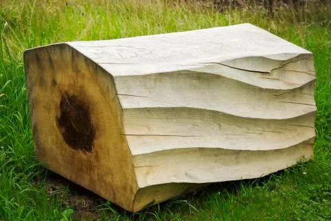 Close up of carved piece of tree trunk with wave pattern lying on grass. 스톡 사진