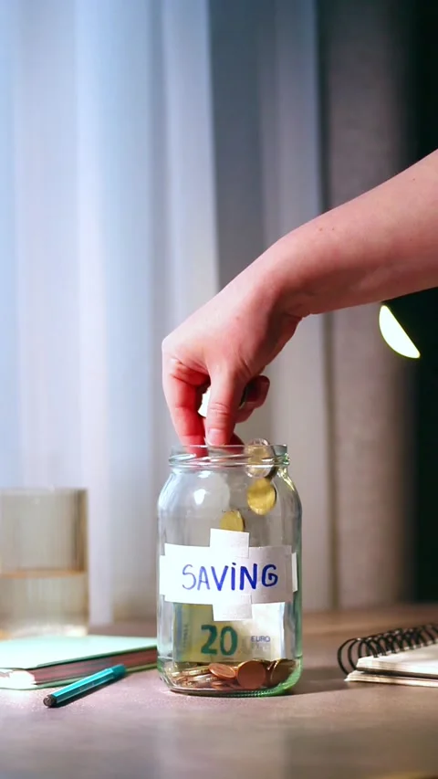 Close up of cash being added to transparent money jar. Represents traditional Stock-Footage 329687729