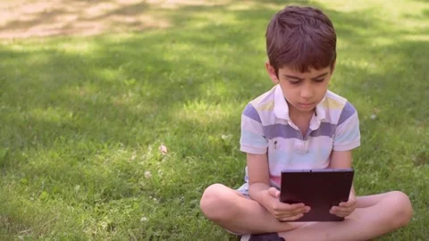 Close up Caucasian little boy using Digital Tablet sitting on the grass outdoors Stock Footage 211403480