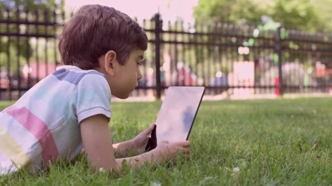 Close up Caucasian little boy using Digital Tablet sitting on the grass outdoors Stock Footage 211403836