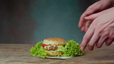 Close up of Caucasian Man's Hands Take a juicy Burger from a wooden table Video stock 234899744