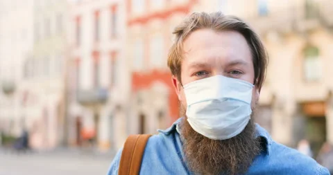 Close up of Caucasian young man with beard and in medical mask looking at camera Stock Footage 130485312