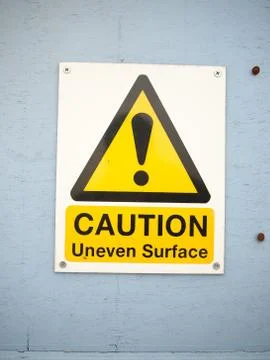 A close up caution uneven surface sign on blue wall seafront Stock Photos