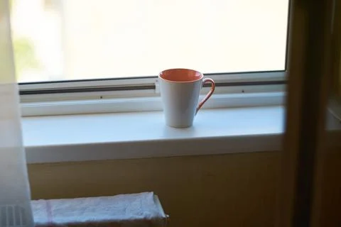 Close-up of ceramic coffee mug resting on white windowsill in morning light 库存照片