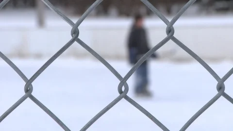 Close Up of Chain Link Fence with Kids Playing Hockey on an Outdoor Skating Rink Stock Footage