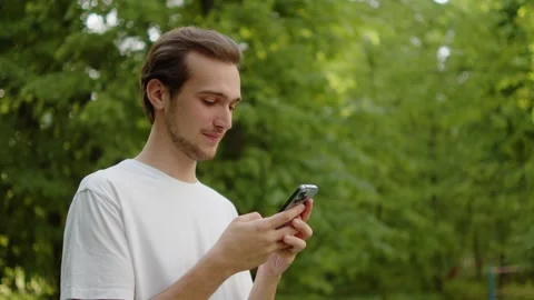 Close up of a cheerful guy in a white t-shirt texting on his mobile phone o.. Stock Footage 335206704