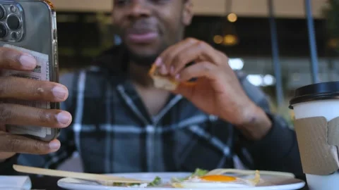Close-up of a cheerful man eating with his hand and looking at the smartphone Video stock 234549639