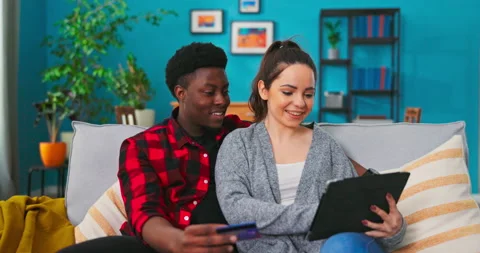 Close up of cheerful nice mixed-races married couple sitting on sofa in modern 库存影片 152352566