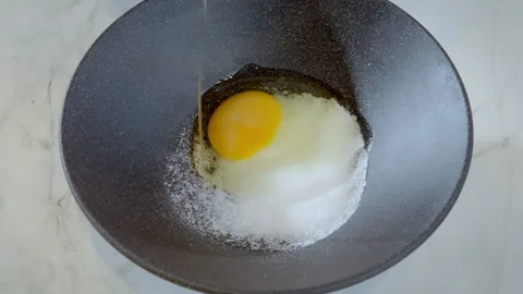 Close-up of chef adding raw egg to bowl with sugar to prepare dessert. Stock Footage 308183135
