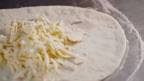 A close-up chef adds cheese to rolled out pizza dough. Stock Footage 167262483