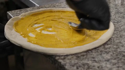 A close-up of the chef applying yellow sauce to the pizza dough in the kitchen. Stock Footage 342702272