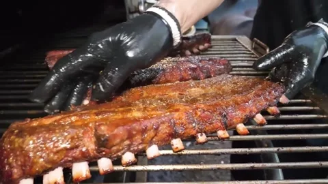 Close-up of Chef in Black Gloves Placing Juicy Grilled BBQ Pork Ribs on a Smoker Stock Footage 338212529