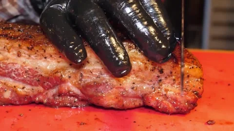Close-up of Chef in Black Gloves Slicing Juicy Grilled BBQ Pork Steak on a Red C Stock Footage 338212683