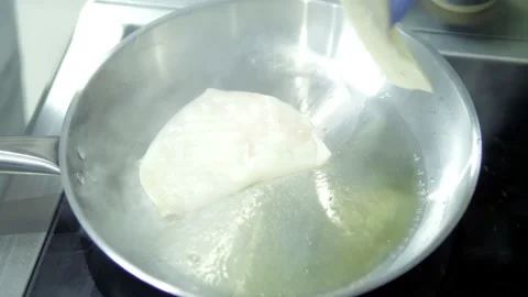 A close-up chef in blue gloves plunges seafood and squid into a hot frying pan Stock Footage 167243470