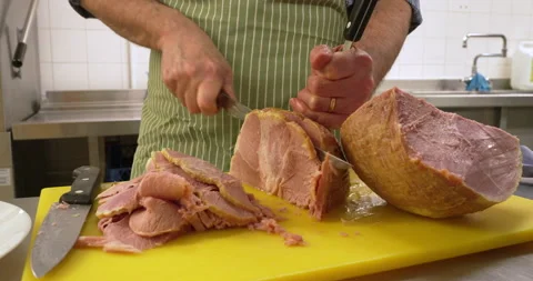Close-up of a chef is carving a large piece of ham on a chopping board Stock Footage 239535012