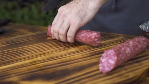 Close up chef cook using knife for cutting sausage pepperoni on slices on wooden Stock Footage 98475499
