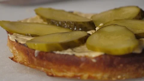 Close-up of a chef cooking a burger, he puts sliced pickles on a bun with sauce. Stock Footage 287580022