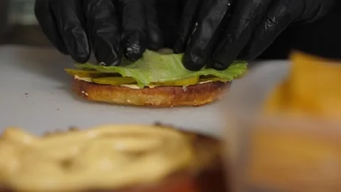 Close-up of a chef cooking a burger, he puts sliced pickles on a bun with sauce. Stock Footage 343736333