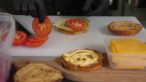 Close-up of a chef cooking a burger, puts a slice of tomato on a bun with sauce. Vídeo Stock 343736381