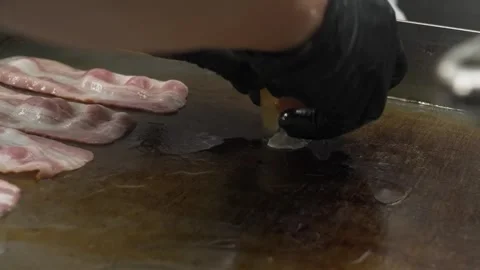 Close-up of Chef Cracking Egg Onto Hot Griddle Next to Raw Bacon Strips Stock Footage 331633844