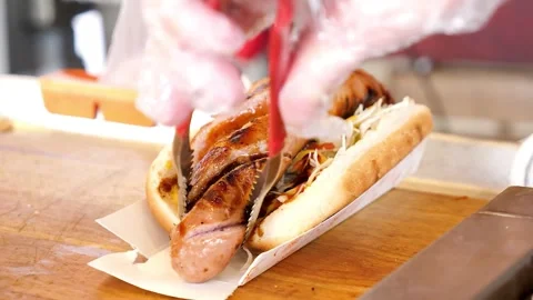 Close-up of a chef cutting a grilled bratwurst sausage in a bun with scissors Stock Footage 331954548