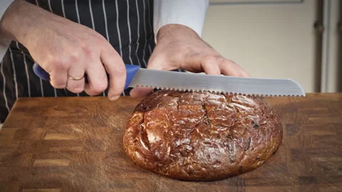 Close-up of a chef cutting a loaf of dark bread in half on a wooden board. Video stock 304794485